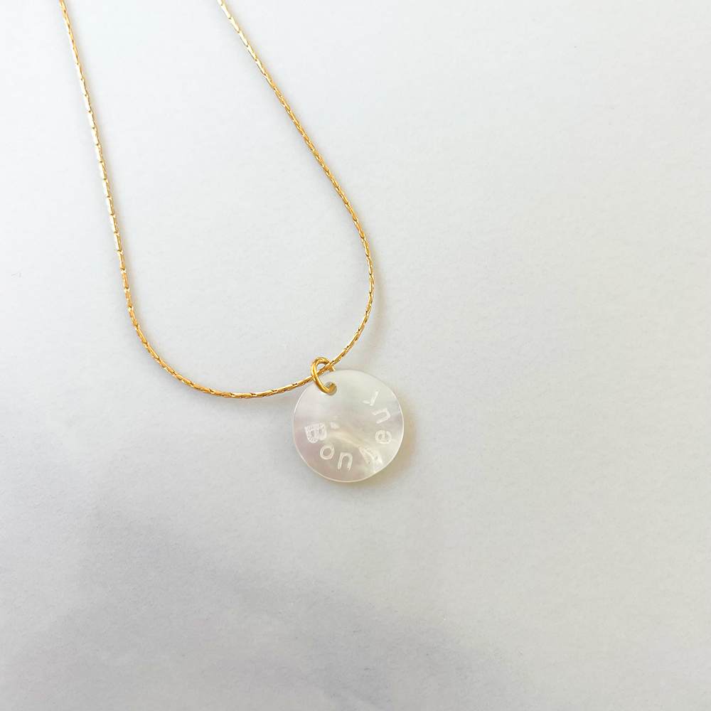 Un collier en acier inoxydable robuste avec un pendentif en nacre délicat affichant le mot "bonheur" avec élégance. La combinaison de l'acier et de la nacre crée un contraste saisissant, symbolisant à la fois la force et la douceur de la quête du bonheur. Un accessoire raffiné qui incarne l'harmonie entre la modernité et la simplicité intemporelle.