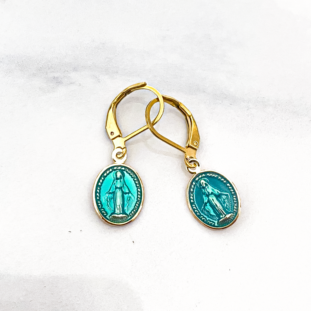 La photo présente une paire de boucles d'oreilles bleues, délicates et élégantes, qui captent instantanément le regard. Chaque boucle est ornée d'une représentation minutieuse de la Vierge Marie, évoquant une aura de spiritualité et de grâce. La teinte bleue douce ajoute une touche de sérénité à l'ensemble, tandis que les détails fins ajoutent une dimension de beauté artisanale. Ces boucles d'oreilles semblent prêtes à porter un symbole de foi et d'élégance à toute tenue avec leur charme intemporel.