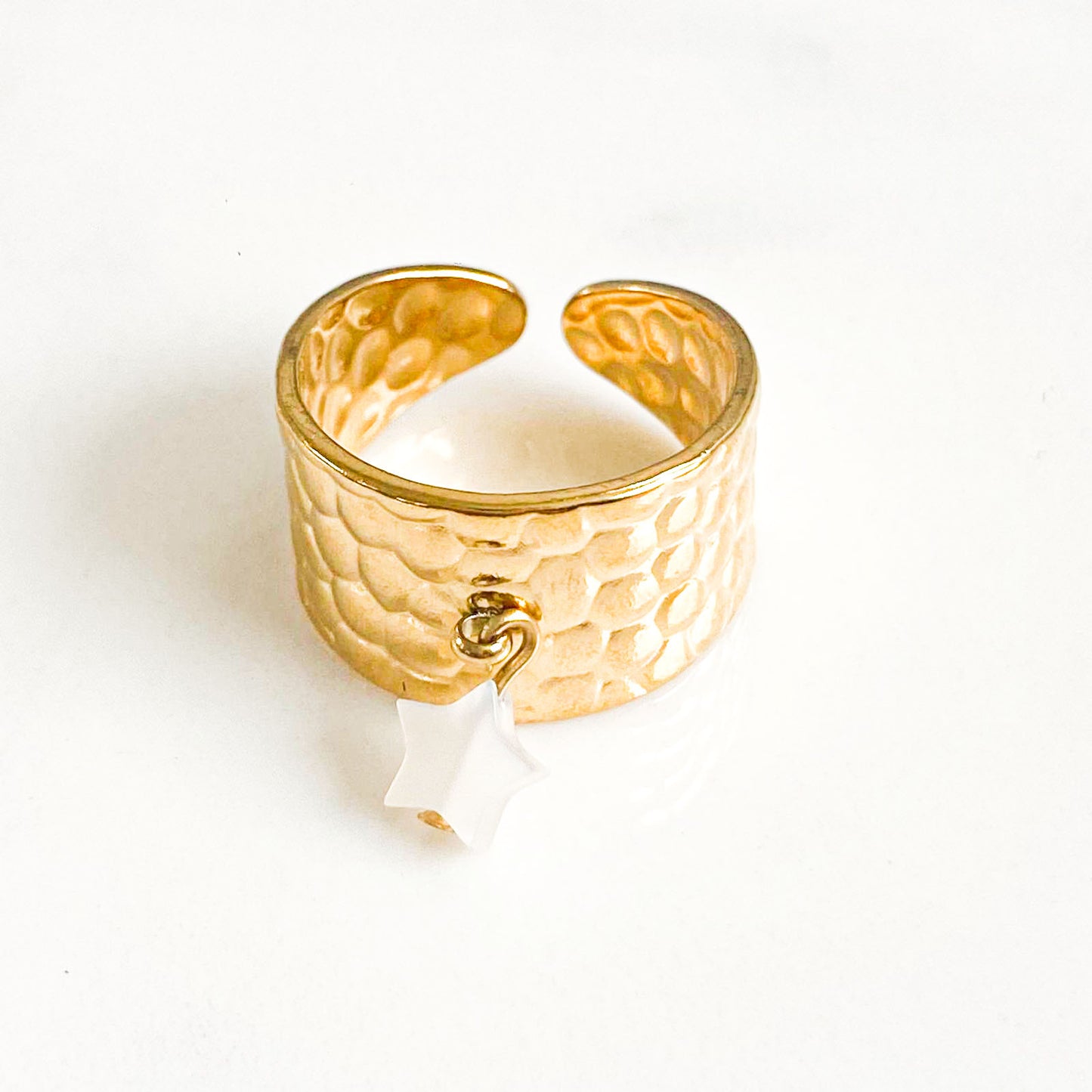 La photo capture une bague en acier inoxydable, minimaliste et élégante. Son charme est accentué par un délicat pendentif en forme d'étoile, sculpté dans de la nacre, ajoutant une touche de sophistication naturelle. Cette combinaison crée un contraste saisissant entre la robustesse de l'acier et la délicatesse de la nacre, capturant l'essence de l'équilibre entre force et grâce.