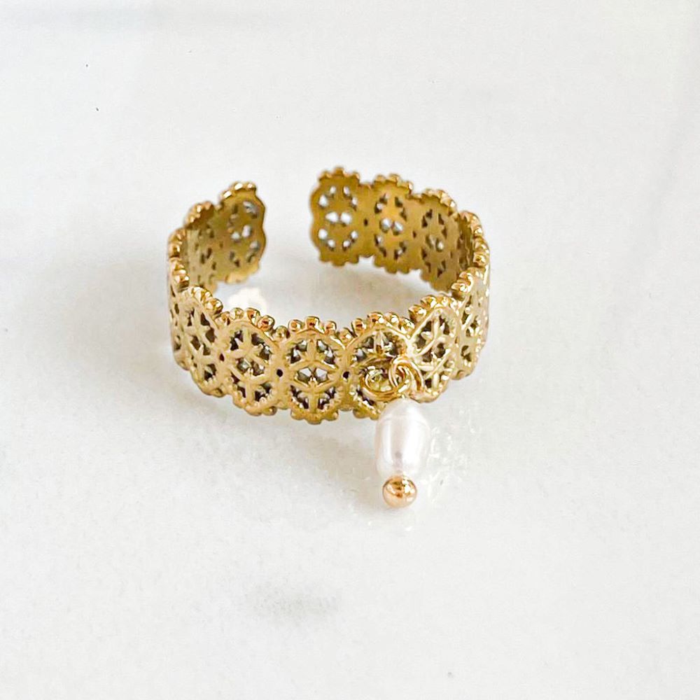 La photo montre une bague ajustable en acier inoxydable finement ciselée, ornée d'une perle d'eau. Cette bague est conçue pour résister à l'eau, ce qui en fait un accessoire idéal pour être porté tout au long de l'été, même pendant les baignades. La perle d'eau apporte une touche élégante et naturelle au design de la bague. Un aspect notable est que tous les bijoux de cette marque sont créés et assemblés en France, ce qui souligne un engagement envers la qualité et le savoir-faire artisanal.