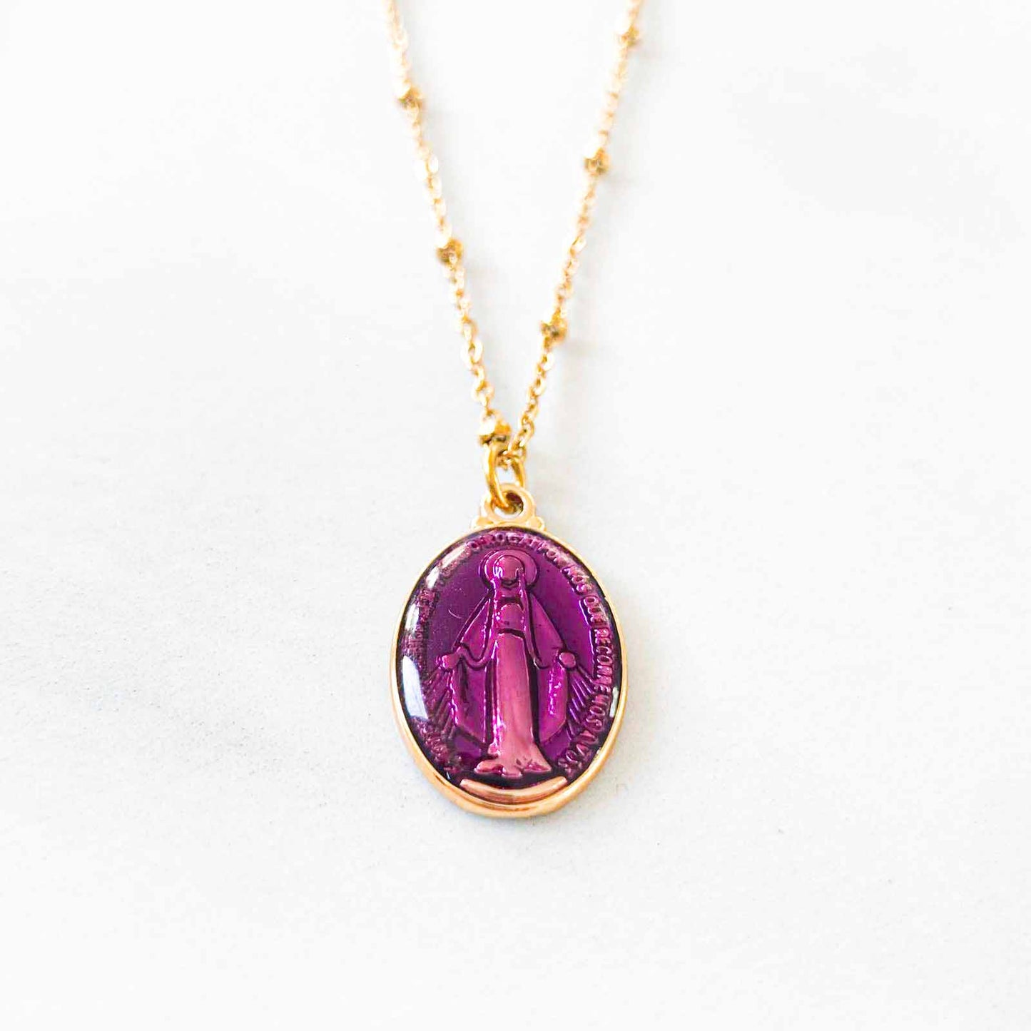 Un collier en acier inoxydable brille sous la lumière, avec des maillons lisses et robustes. Son pendentif violet, vierge de toute inscription, semble flotter délicatement, contrastant avec l'acier froid. L'ensemble incarne une élégance minimaliste, prêt à être personnalisé par celle qui le porte.