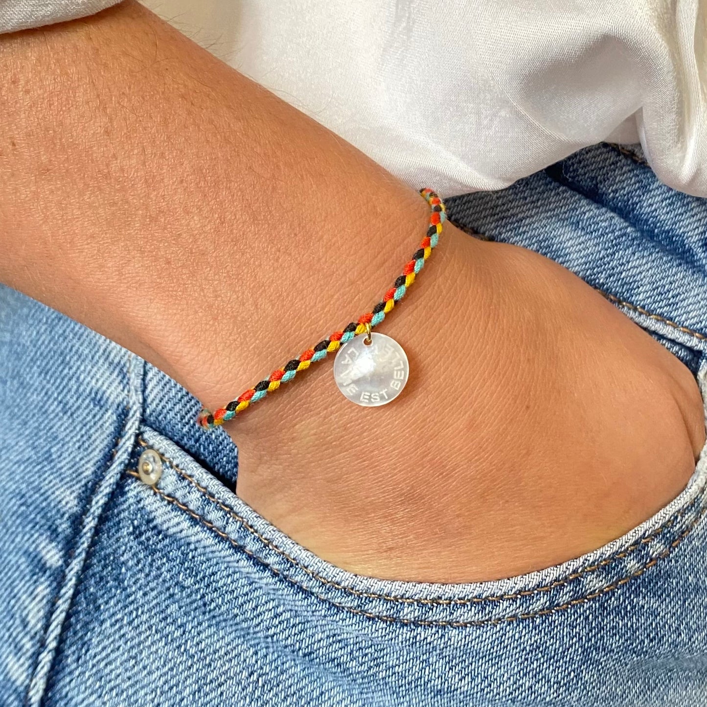 Un bracelet cordon vibrant et multicolore, accentué par un pendentif en nacre arborant le mot "chance". La palette de couleurs évoque la joie et la vivacité, tandis que le pendentif ajoute une touche de délicatesse et de positivité, évoquant l'espoir et les opportunités à saisir. L'ensemble incarne une fusion harmonieuse entre l'esthétique ludique et le symbolisme inspirant.