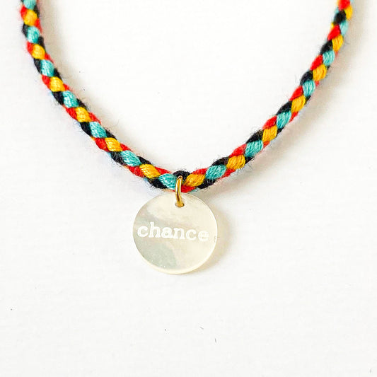 Un bracelet cordon vibrant et multicolore, accentué par un pendentif en nacre arborant le mot "chance". La palette de couleurs évoque la joie et la vivacité, tandis que le pendentif ajoute une touche de délicatesse et de positivité, évoquant l'espoir et les opportunités à saisir. L'ensemble incarne une fusion harmonieuse entre l'esthétique ludique et le symbolisme inspirant.