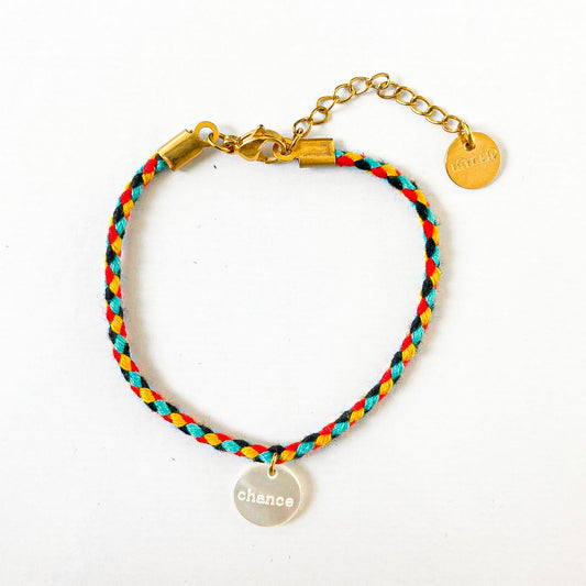 Un bracelet cordon vibrant et multicolore, accentué par un pendentif en nacre arborant le mot "chance". La palette de couleurs évoque la joie et la vivacité, tandis que le pendentif ajoute une touche de délicatesse et de positivité, évoquant l'espoir et les opportunités à saisir. L'ensemble incarne une fusion harmonieuse entre l'esthétique ludique et le symbolisme inspirant.