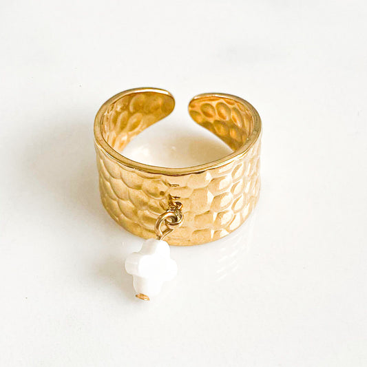 La photo présente une bague ajustable en acier inoxydable, dont le design est simple et élégant. Au centre de la bague, il y a un pendentif en forme de trèfle, fabriqué à partir de nacre. La nacre apporte une touche de luminosité et de délicatesse à l'ensemble, créant un contraste intéressant avec le métal robuste de la bague.