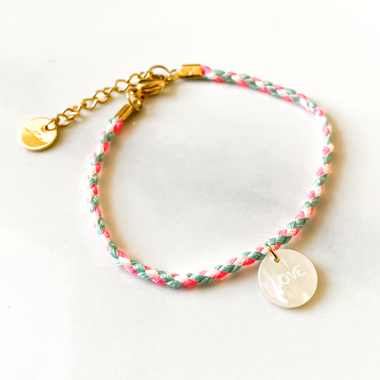 un délicat bracelet cordon rose, orné d'un pendentif en nacre sculpté avec le mot "Love". L'ensemble est présenté dans une élégante boîte assortie, offrant une touche de romantisme et de raffinement à toute occasion.