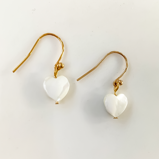 La photo représente des boucles d'oreilles en acier inoxydable muni d'un pendentif coeur en nacre